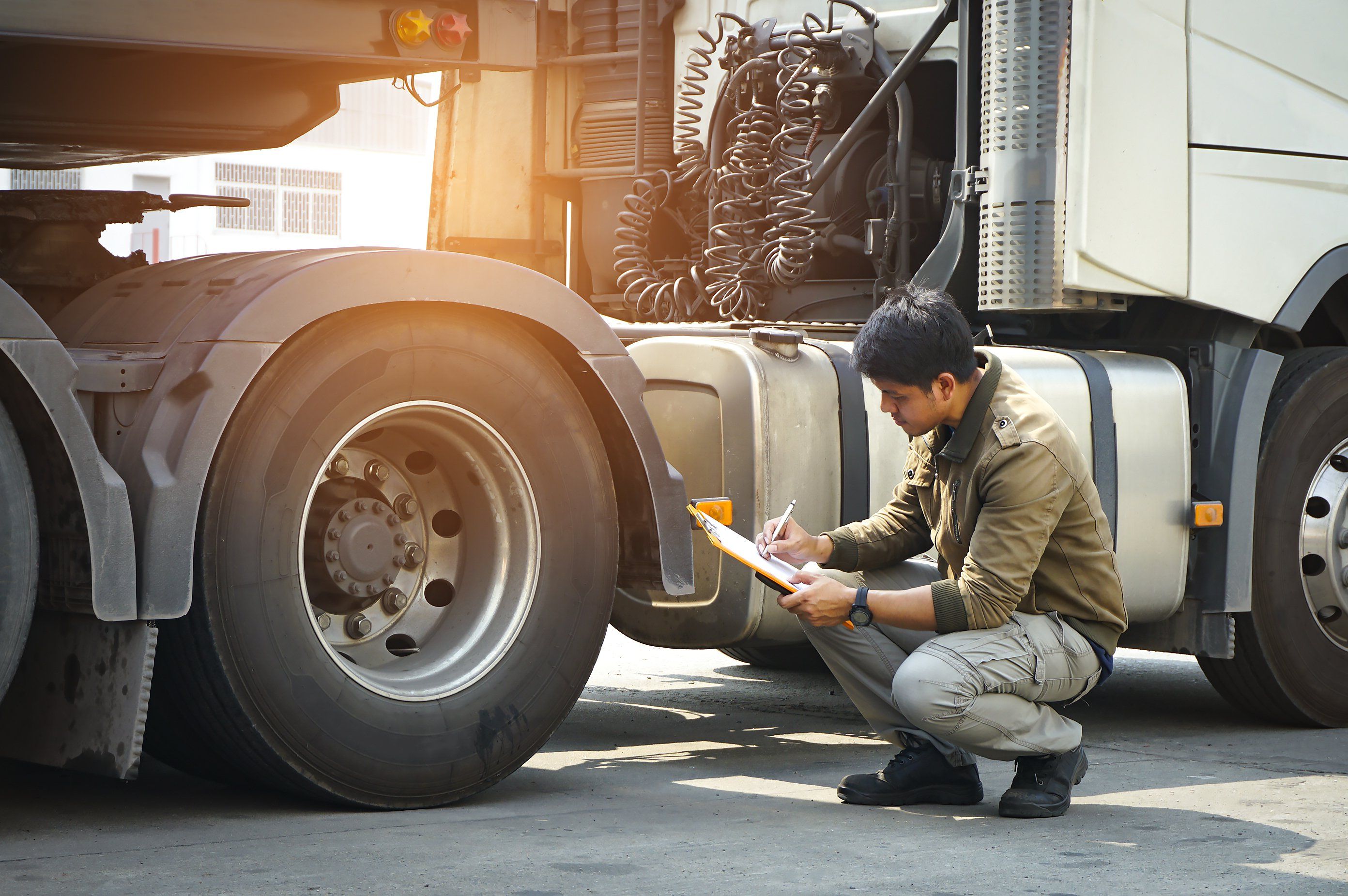 A man with a clipboard kneels down and inspects truck tires.