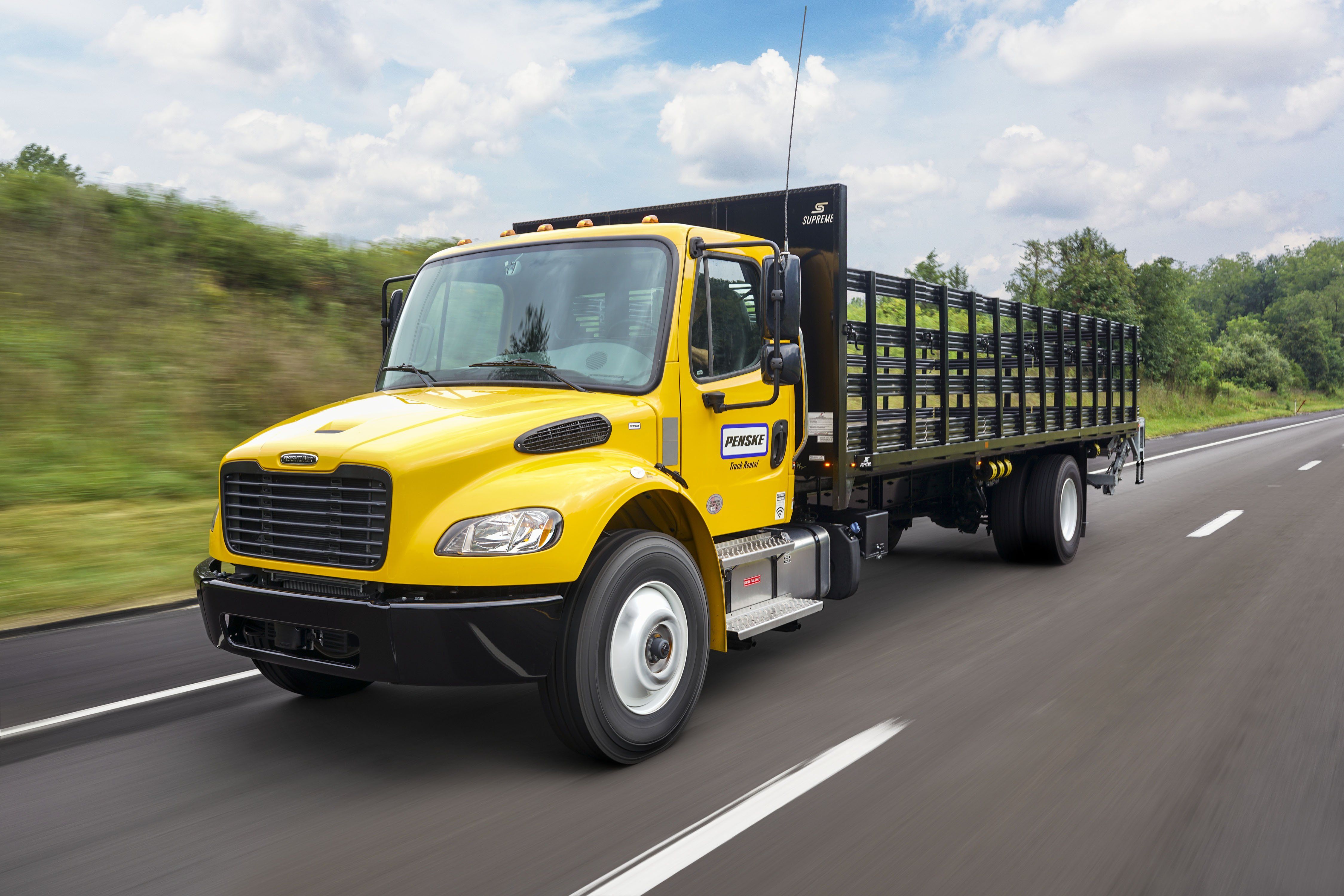 A yellow Penske flatbed truck drives on the highway.