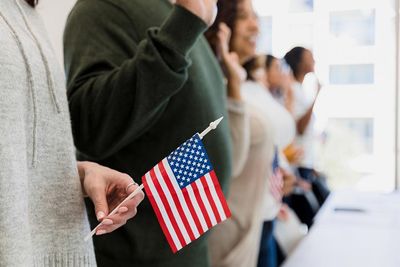 A diverse group of people stand holding small U.S. flags and taking an oath.